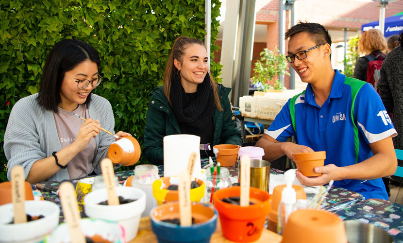 Students laughing and painting pot plants